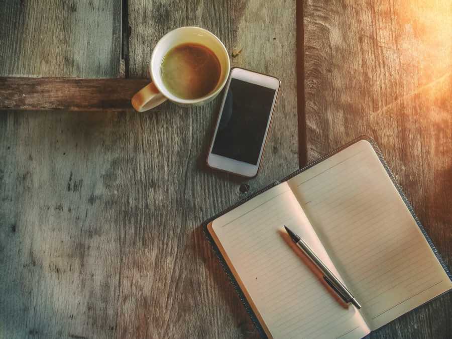 Mesa com café, telemóvel e caderno, pronta para organizar o dia